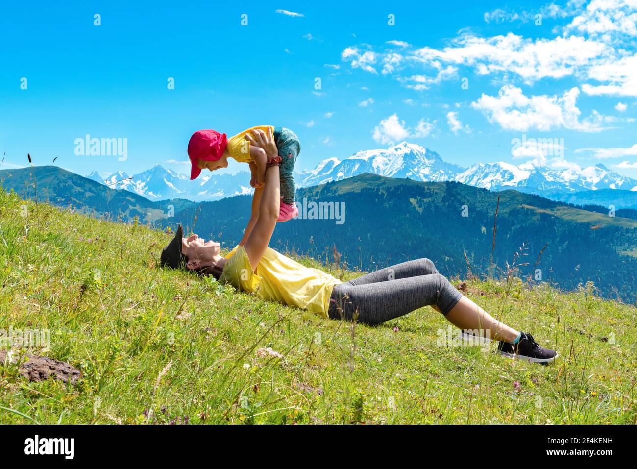 Mutter, die auf Gras im Col des Aravis, Haute-Savoie, Frankreich liegt, das Mädchen abholt Stockfoto