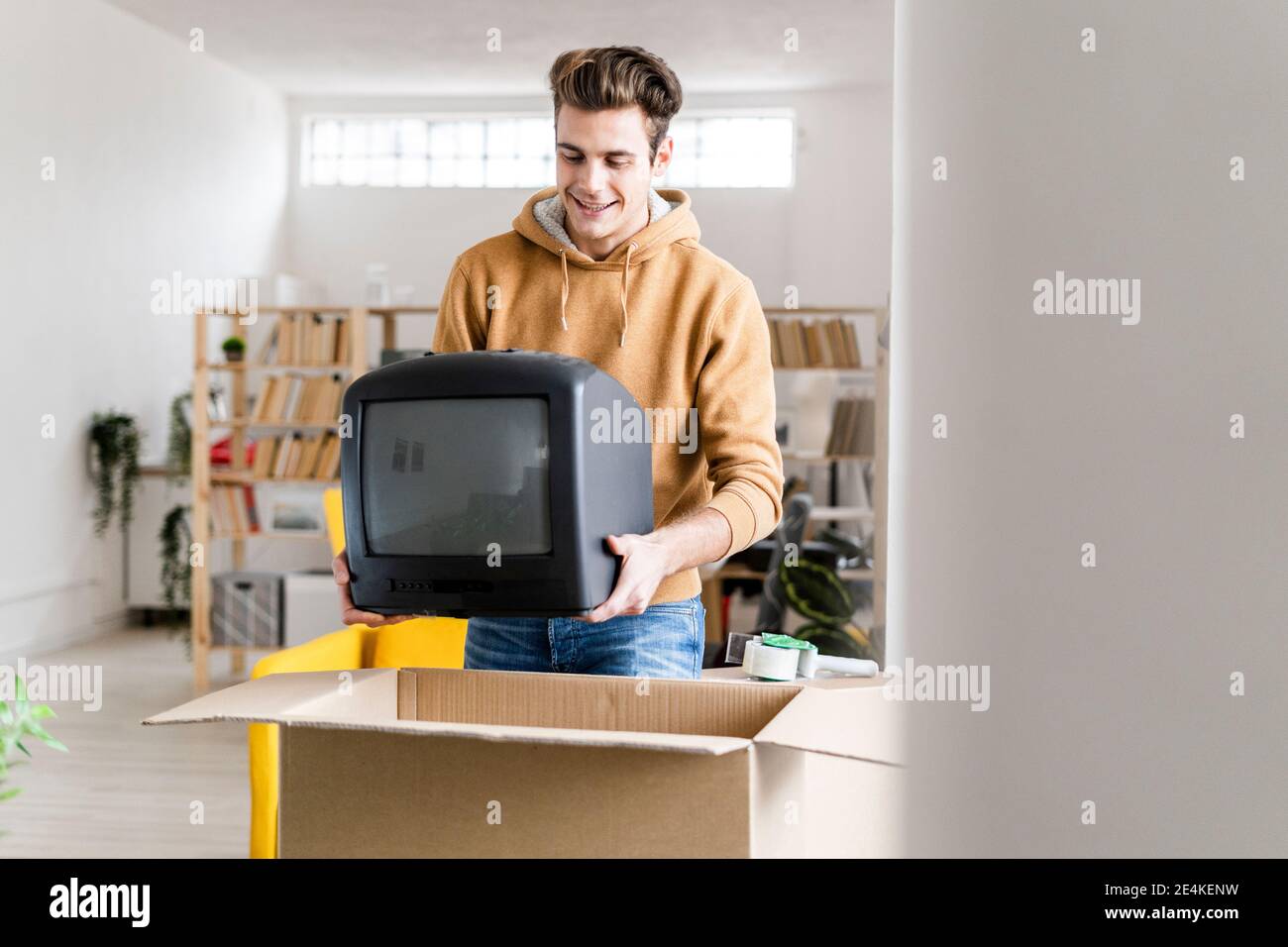 Junger Mann beim Bewegen Fernseher in Pappkarton packen In ein neues Zuhause Stockfoto