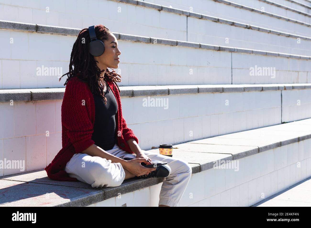 Nachdenklich junge weibliche Millennial sitzen mit Smartphone und wiederverwendbar pokal auf der Treppe an sonnigen Tag Stockfoto