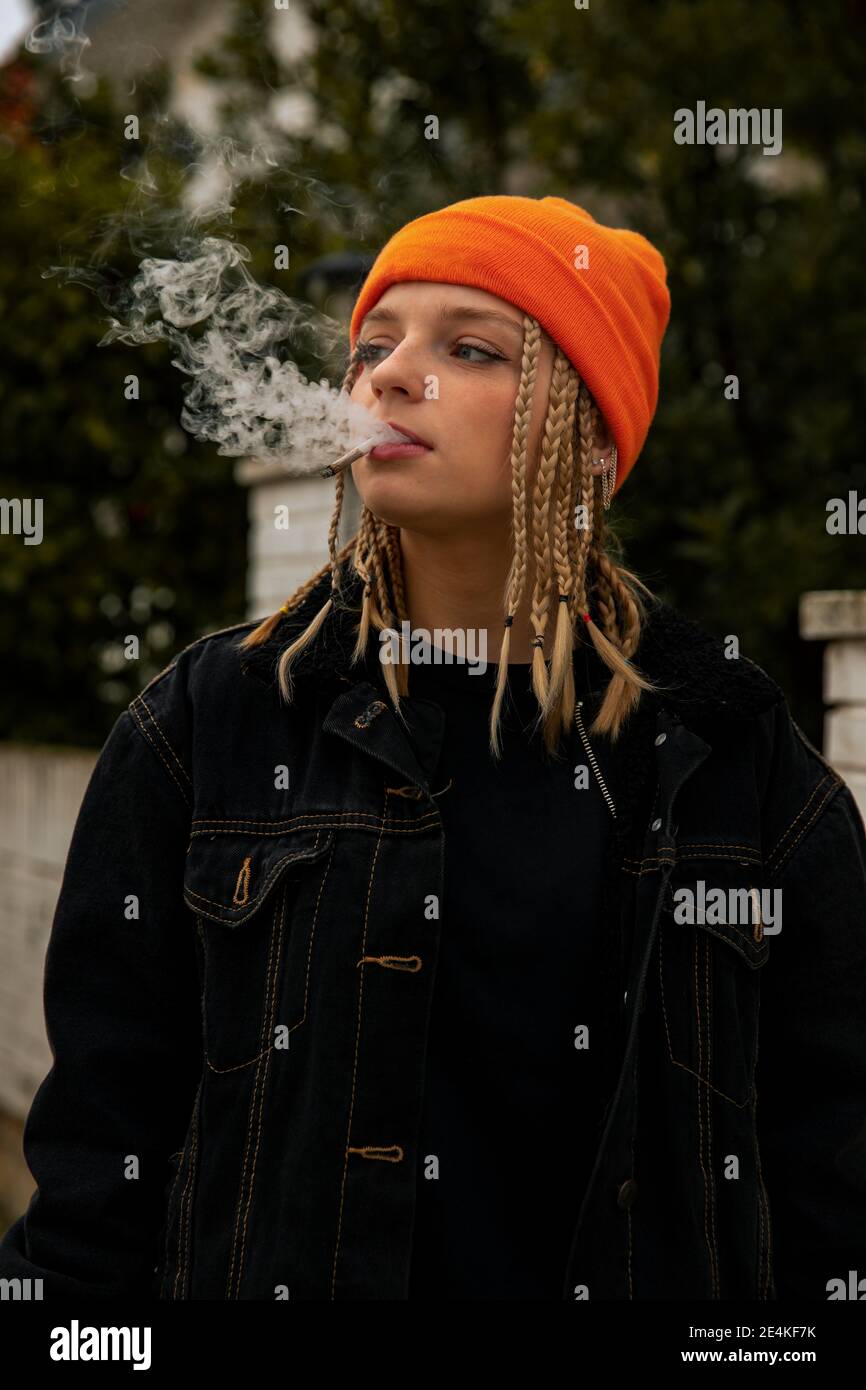Modische Frau trägt schwarze Jacke weg schauen, während Rauchen Zigarette Stockfoto