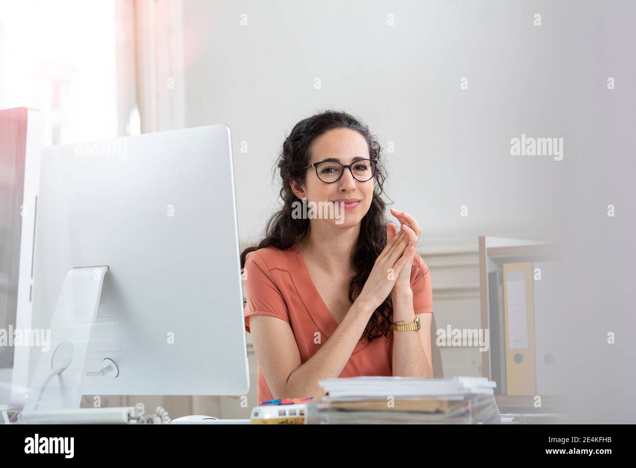 Weibliche professionelle mit Händen zusammengeklemmt sitzen von Computer Stockfoto Weibliche professionelle mit Händen zusammengeklemmt sitzen von Computer Stockfoto