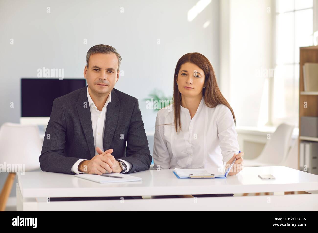 Geschäftsleute, die am Schreibtisch sitzen und die Kamera betrachten Während eines Arbeitsmeeting oder Interviews Stockfoto