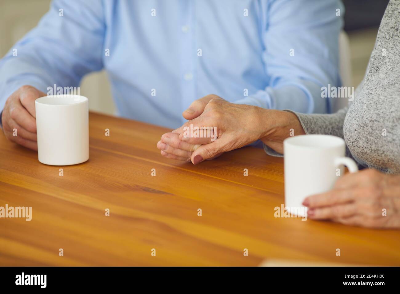 Ein verliebter älterer Partner hält sich die Hände, während er am Tisch sitzt Und eine Tasse Tee genießen Stockfoto