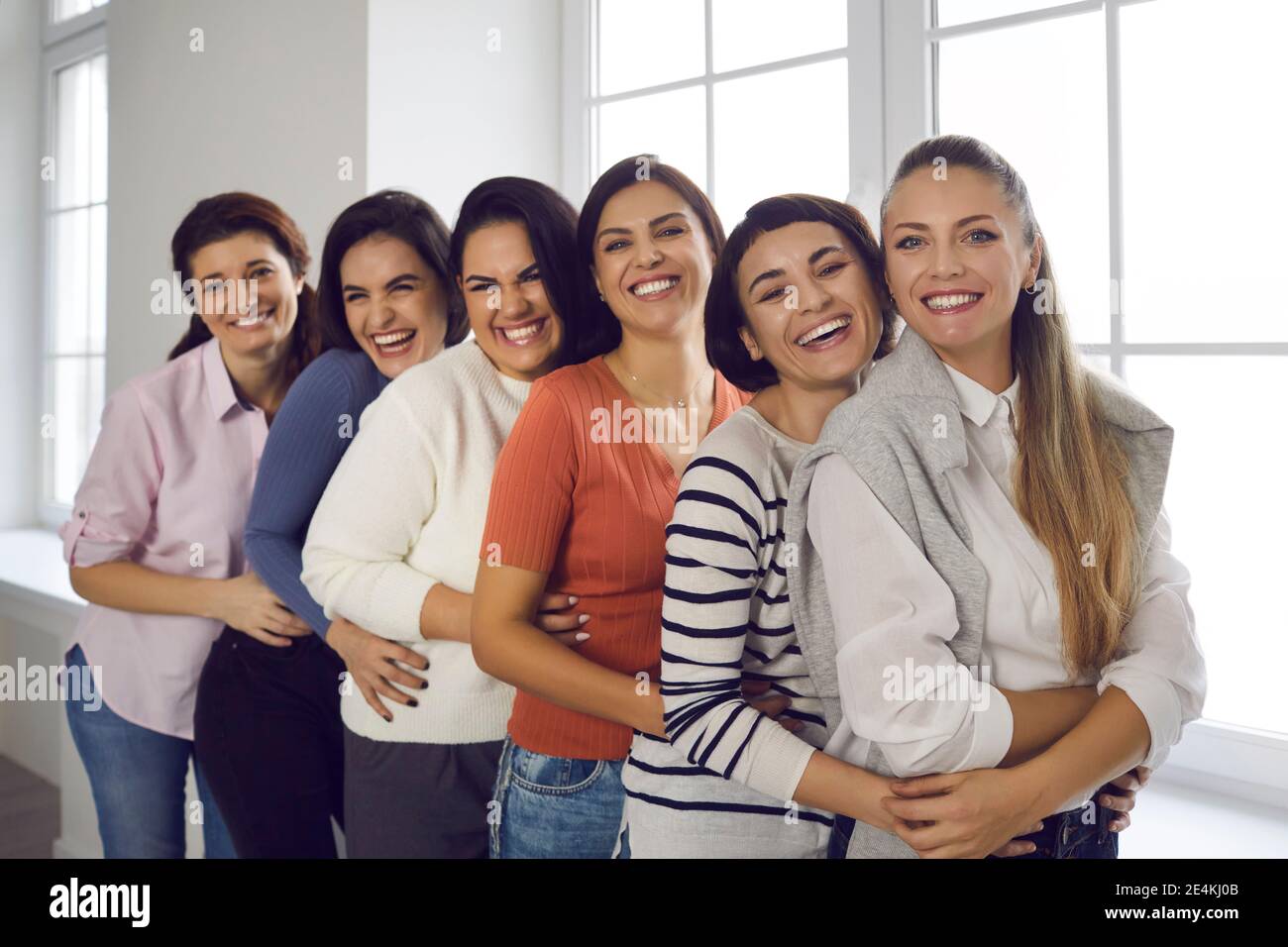 Team von fröhlichen jungen Frauen umarmen einander, lächeln und Blick auf die Kamera Stockfoto