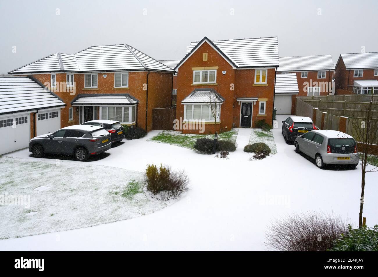 Unberührter Neuschnee bedeckt Straßen, Wege, Autos und Gras auf einer modernen Wohnsiedlung in Lancashire, Großbritannien Stockfoto