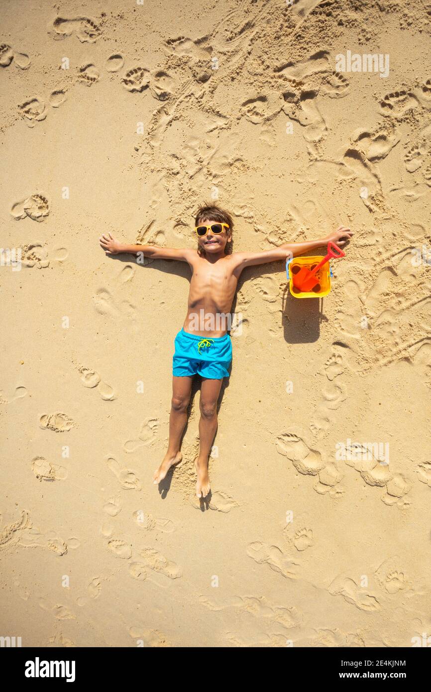 Glücklicher 10 Jahre alter Junge, der entspannt am Strand liegt Mit Schaufelansicht von oben Stockfoto