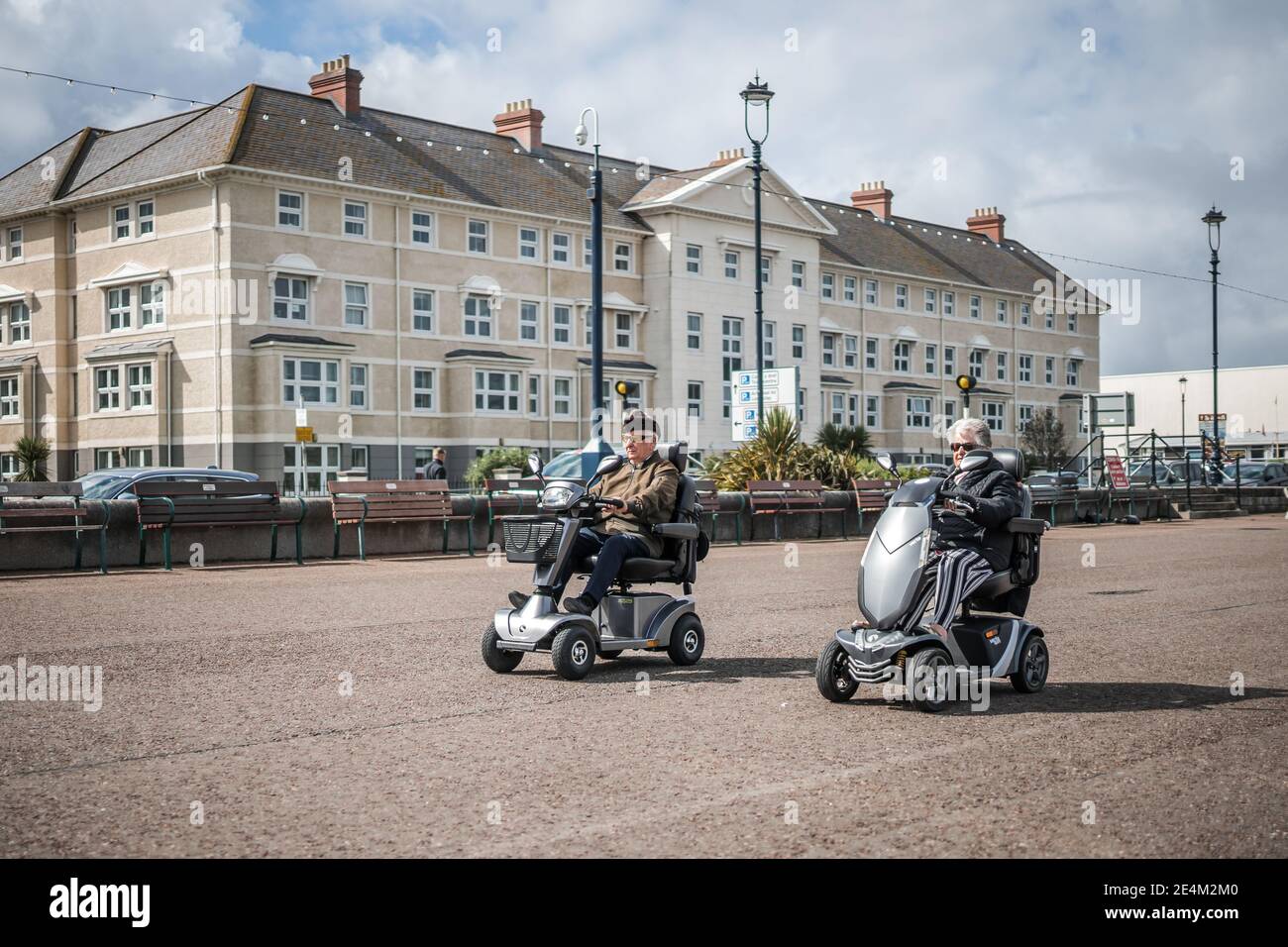 Zwei Rentner auf Mobilitäts-Scootern, die am Meer entlang fahren Hüte auf Kreuzfahrt entlang Rennen llandudno coole alte Menschen Leute nach Hause zu entkommen Stockfoto