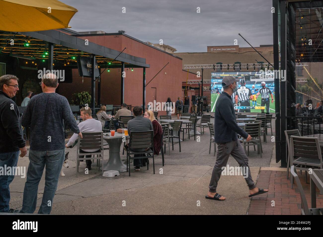 Bar mit Sitzgelegenheiten im Freien während der Covid-19 Pandemie. Gönner sind sozial distanziert & einige werden beim Betrachten eines Fußballspiels maskiert. Stockfoto