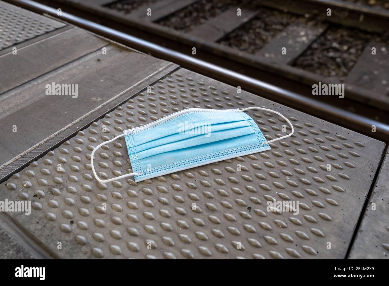 Medizinische blaue Gesichtsmaske auf einem Bahnsteig mit Schienen und einem Gleisbett im Hintergrund. Einweg-Schutz am Bahnhof. Stockfoto