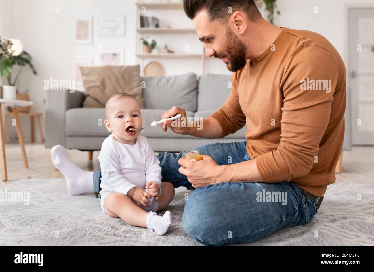 Glücklich Papa Löffel Fütterung Kleinkind Sitzt Auf Dem Boden Zu Hause Stockfoto