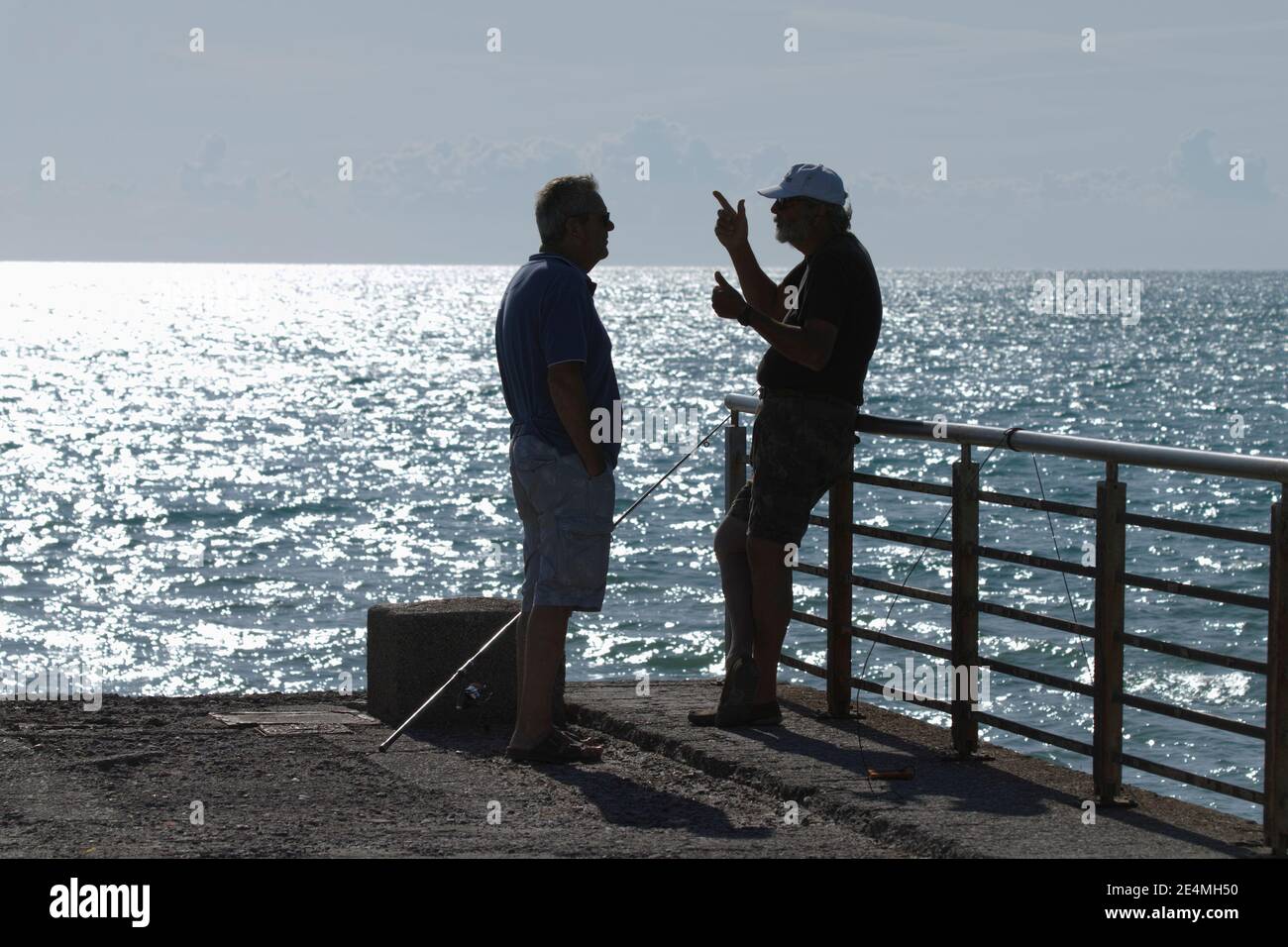Zwei Männer vor glitzerndem Meer reden dramatische Gesten, gestikulieren Stockfoto