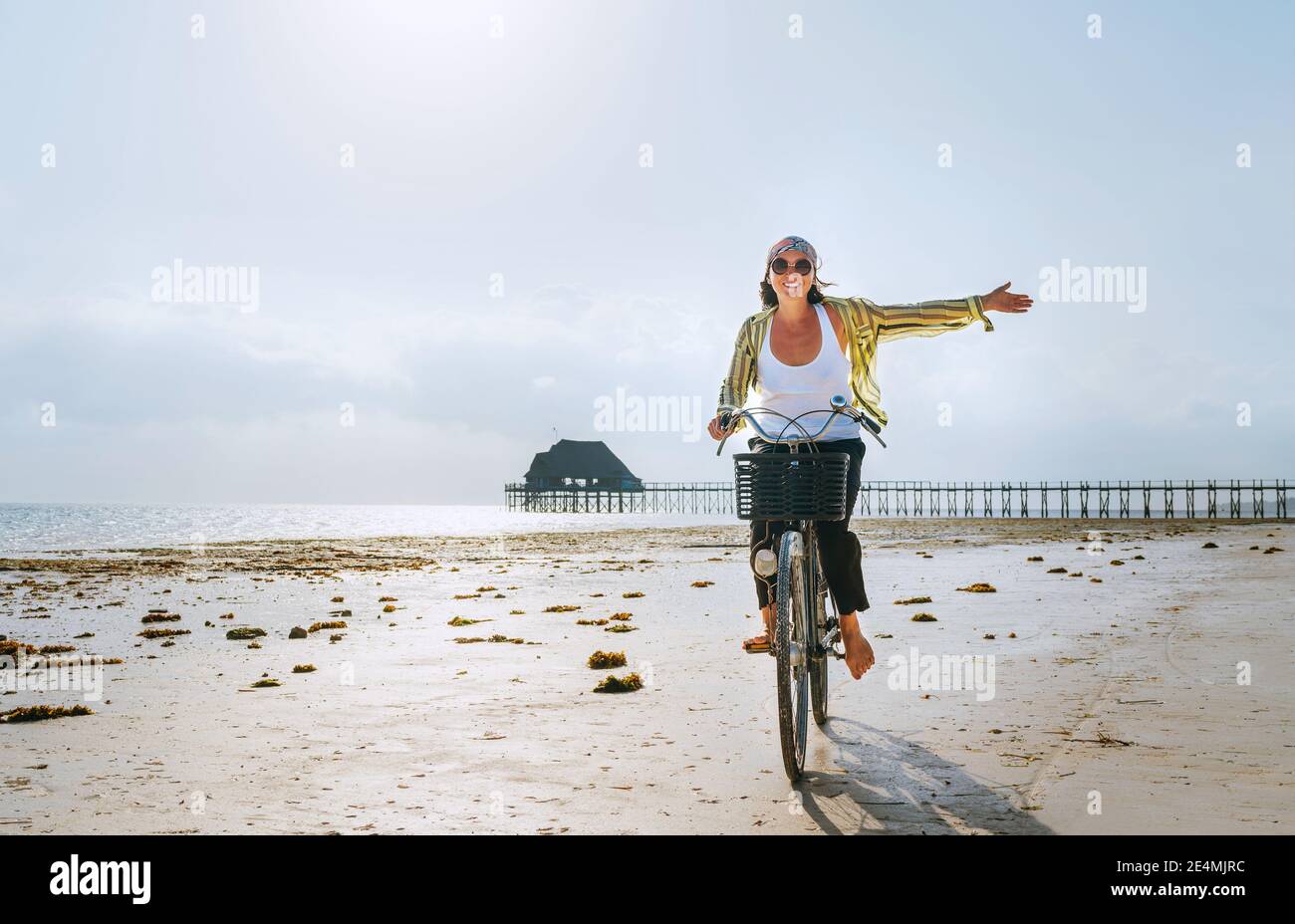 Junge weibliche gekleidete leichte Sommerkleidung freudig warf sie Hand Reiten alte Vintage-Fahrrad mit Vorderkorb auf dem Ebbe Ozean weißen Sand coa Stockfoto