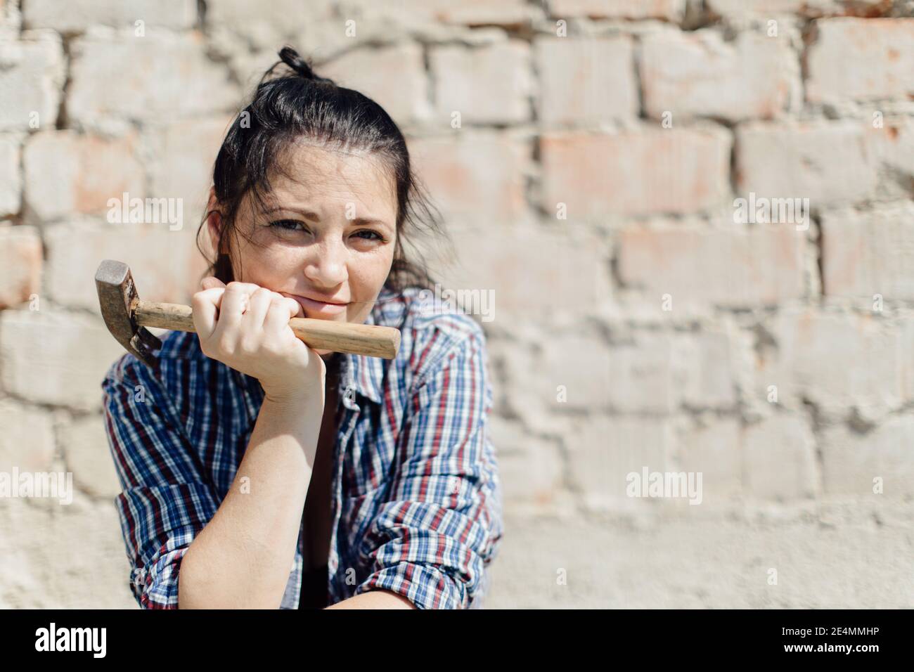 Porträt eines weiblichen Konstrukteuren Kinn auf der Hand mit einem Hammer gegen Ziegelwand Stockfoto