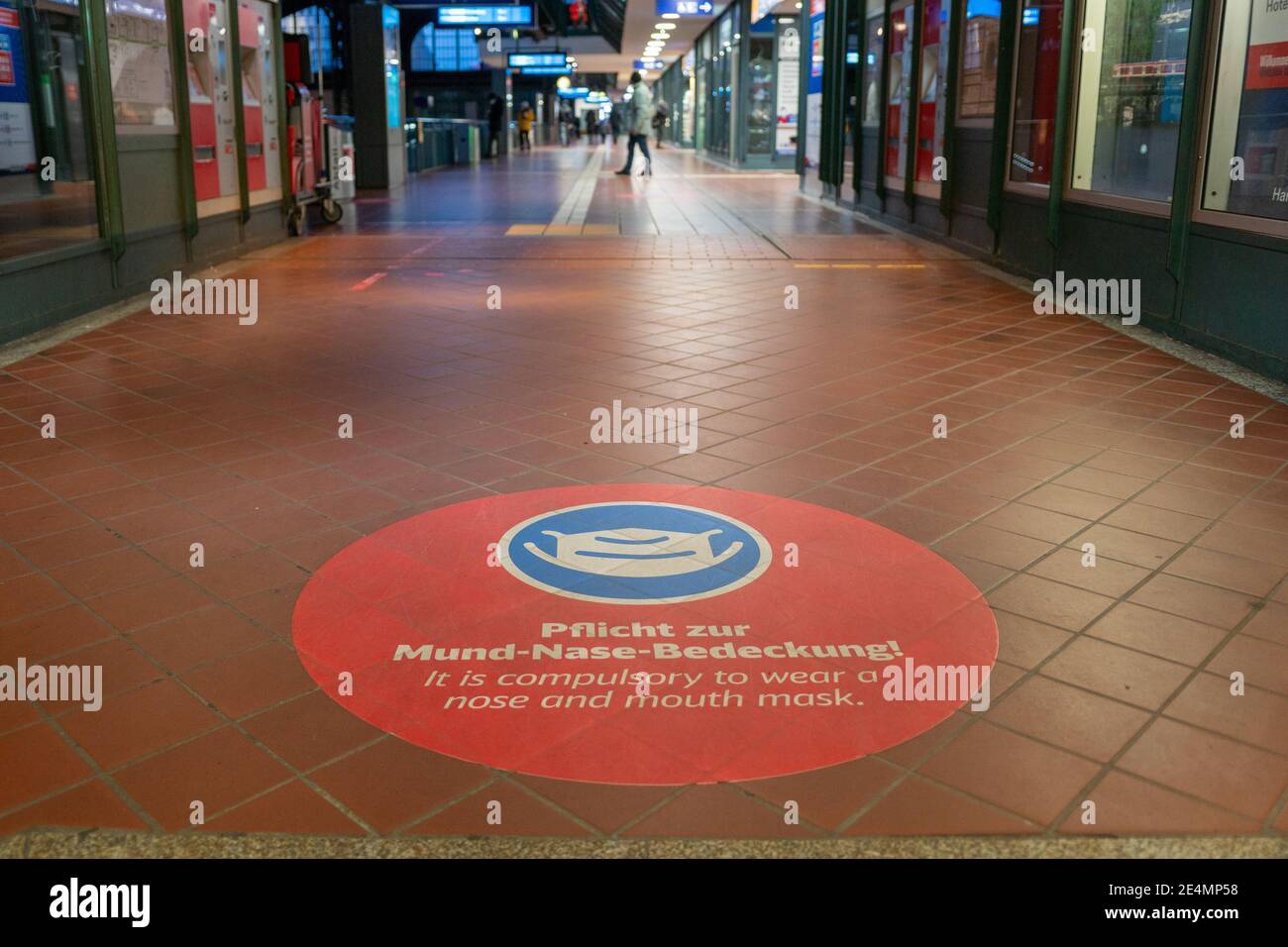 Ausgewählte Fokus auf weißem Gesichtsmaske Symbol, und Bitte decken Sie Ihren Mund und Nase Text, auf rotem Schild auf dem Boden des Bahnhofs in Deutschland während der Socia Stockfoto