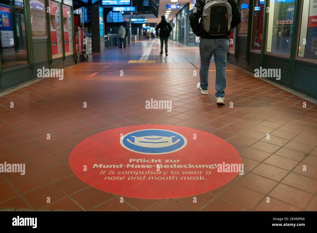 Ausgewählte Fokus auf weißem Gesichtsmaske Symbol, und Bitte decken Sie Ihren Mund und Nase Text, auf rotem Schild auf dem Boden des Bahnhofs in Deutschland während der Socia Stockfoto