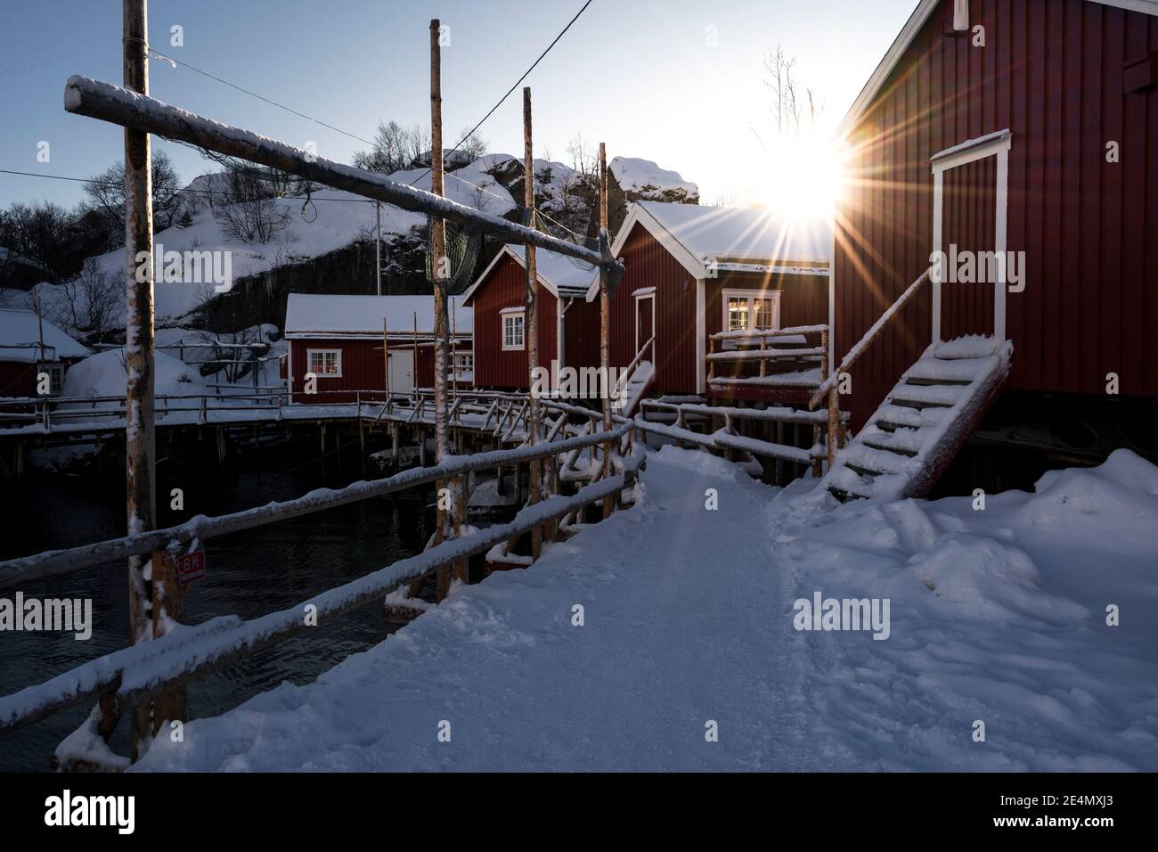 Traditionelle Rorbuer / rote Fischerhütten im kleinen Dorf Nusfjord in Lofoten, Norwegen, während eines kalten Wintersonnenaufgangs. Stockfoto