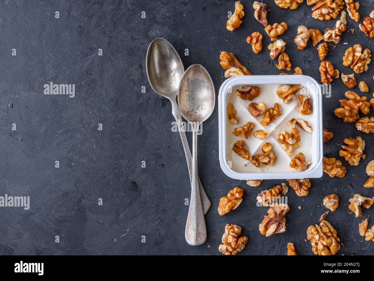 Weißer Joghurt in quadratischer Plastikbecher mit Walnüssen mit Löffeln auf grauem Hintergrund. Flache Ansicht. Stockfoto