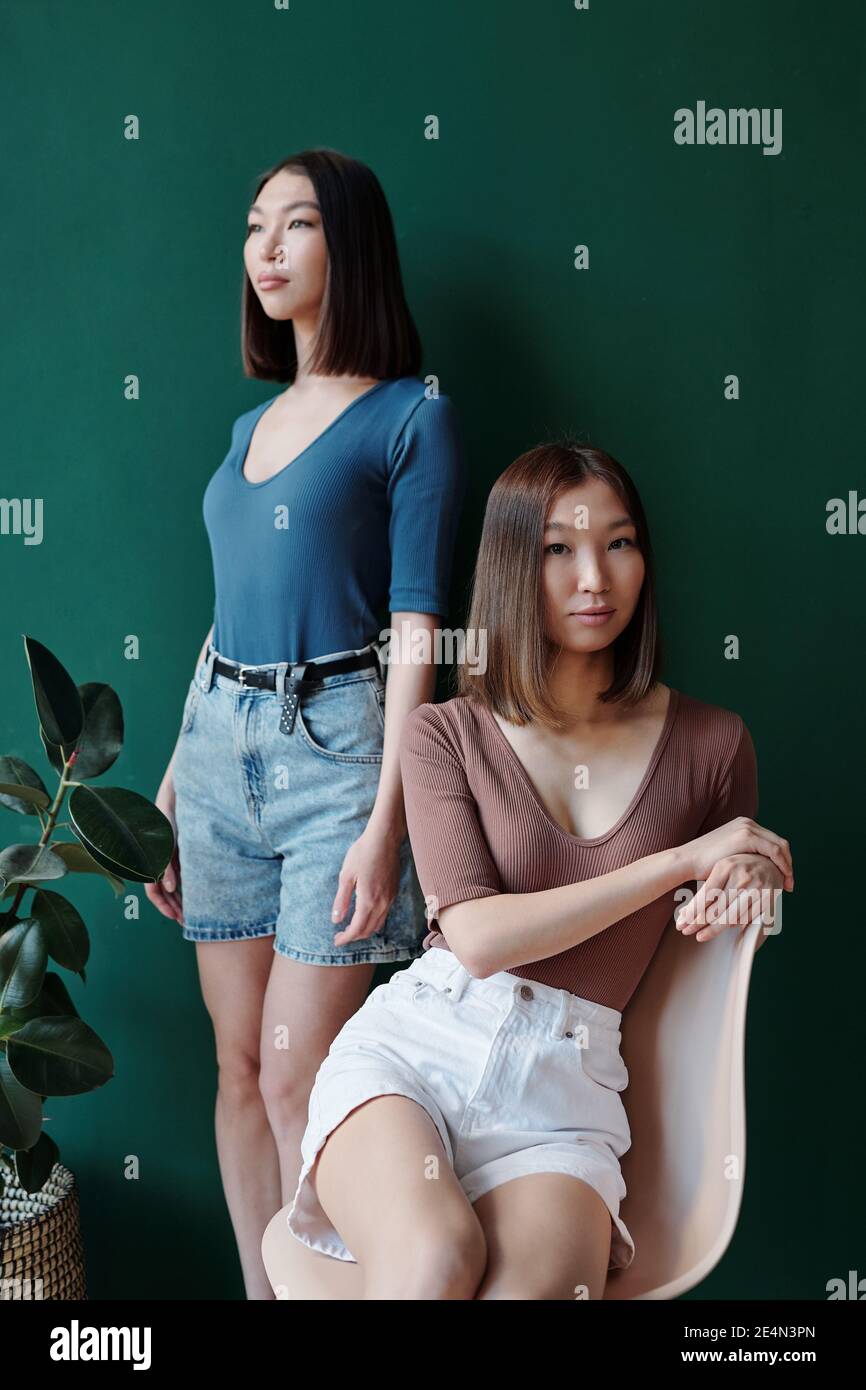 Zwei junge schöne Zwillingsschwestern von asiatischer Ethnie mit dunkel Glattes Haar entspannend vor der Kamera durch häusliche Anlage Im Studio-Umfeld Stockfoto