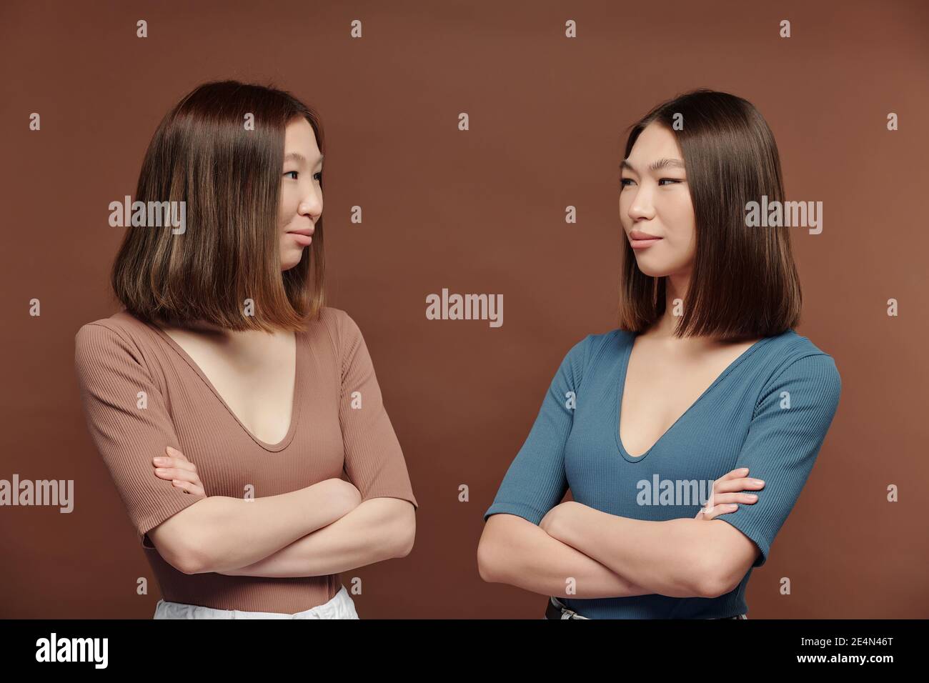 Junge schöne Brünette Zwillingsschwestern in casual Pullovers Blick auf Einander vor der Kamera vor braunem Hintergrund in studio Stockfoto