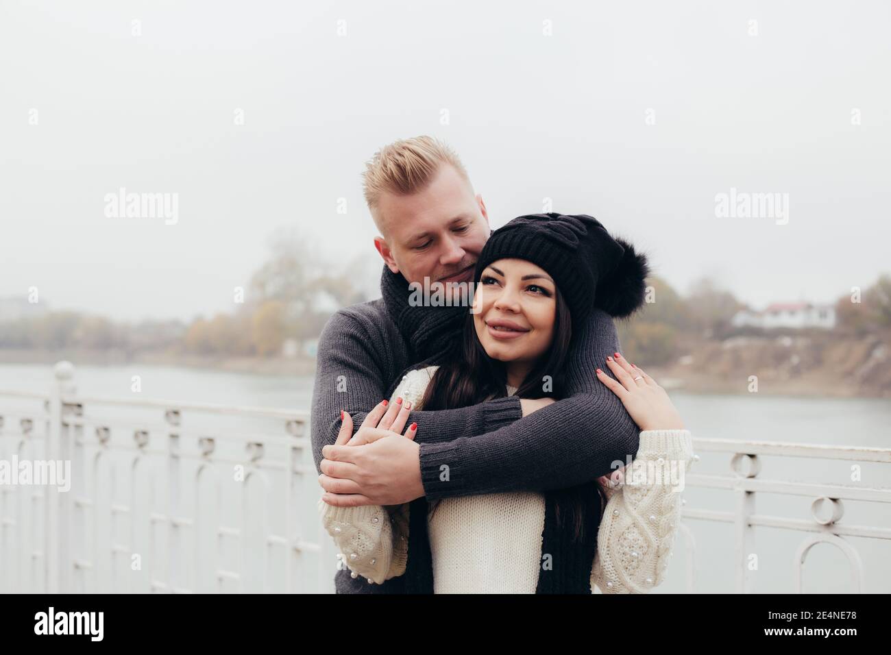 Ein verliebtes Paar geht bei bewölktem Wetter am Ufer entlang, ein Mann umarmt eine Frau vor dem Hintergrund des Flusses. Hochwertige Fotos Stockfoto