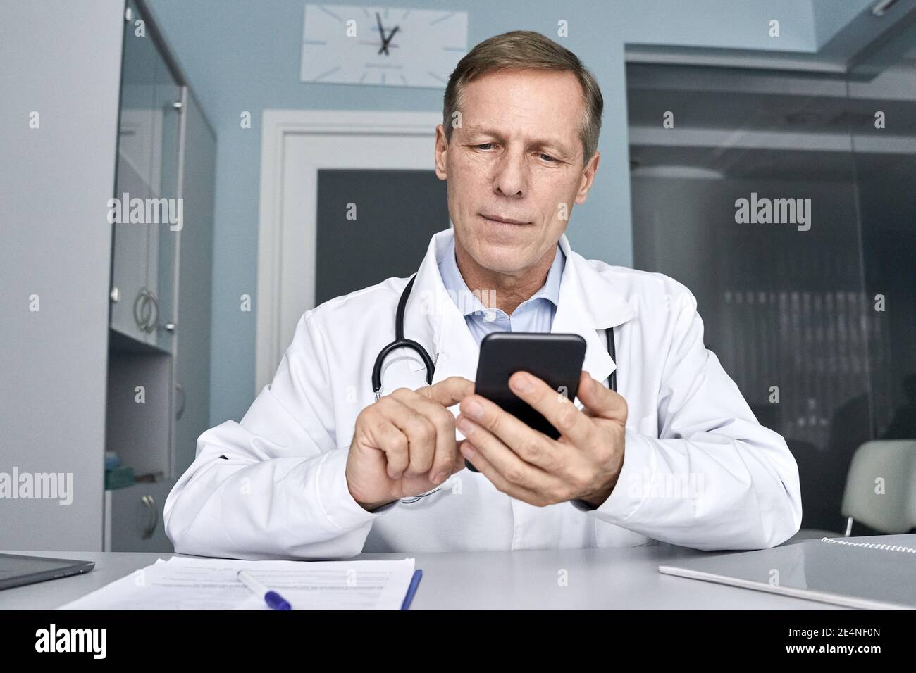 Alter männlicher Arzt hält Handy mit Handy-Telemedizin-Technologie. Stockfoto