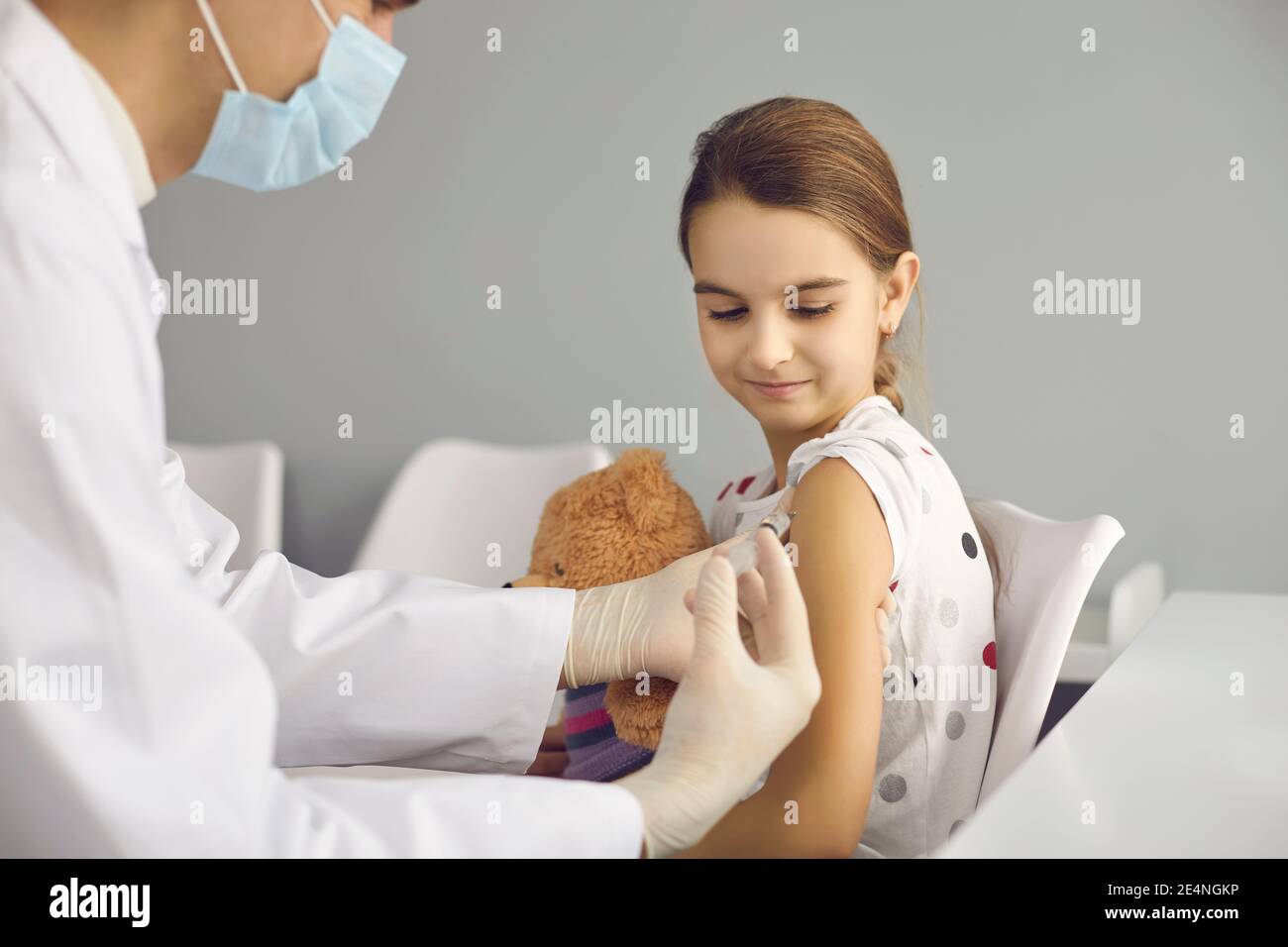 Lächelndes Mädchen Patient sitzen und bekommen Impfung Injektion mit Spritze Gegen Coronavirus Stockfoto