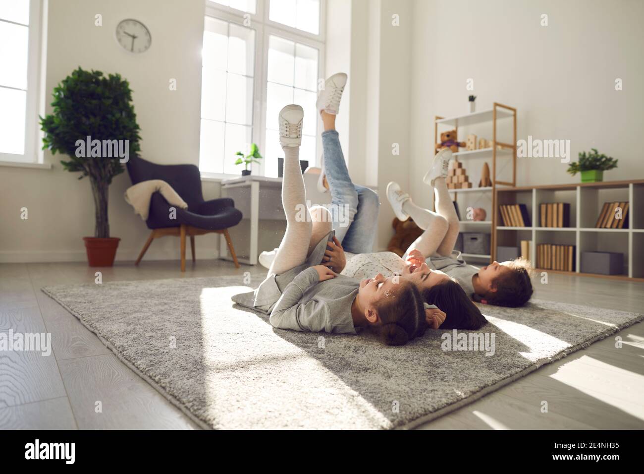 Glückliche, sorglose Mutter und Kinder liegen auf einem warmen Teppich in einem gemütlichen, sonnigen Wohnzimmer Stockfoto