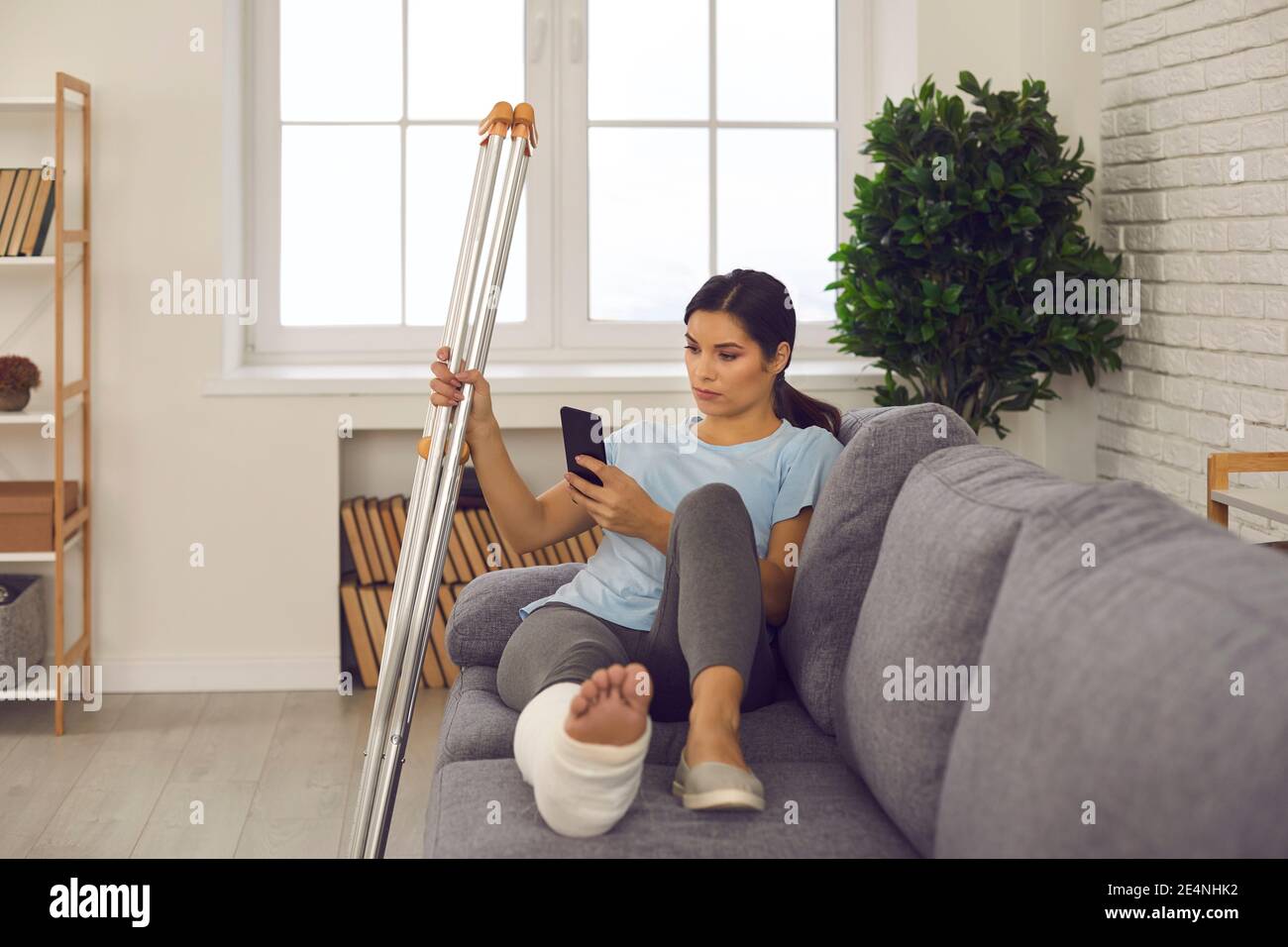 Frau mit gebrochenem Bein mit Handy, lesen Nachrichten online und Leiden allein, nicht in der Lage zu gehen Stockfoto