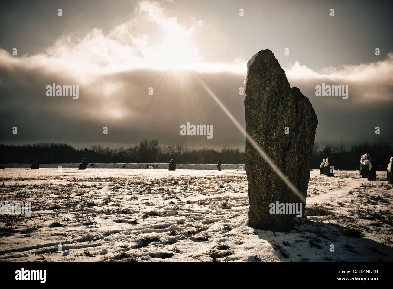 Schwache Wintersonne bricht durch Schneewolken über einem neolithisch stehenden Steinkreis. Stockfoto