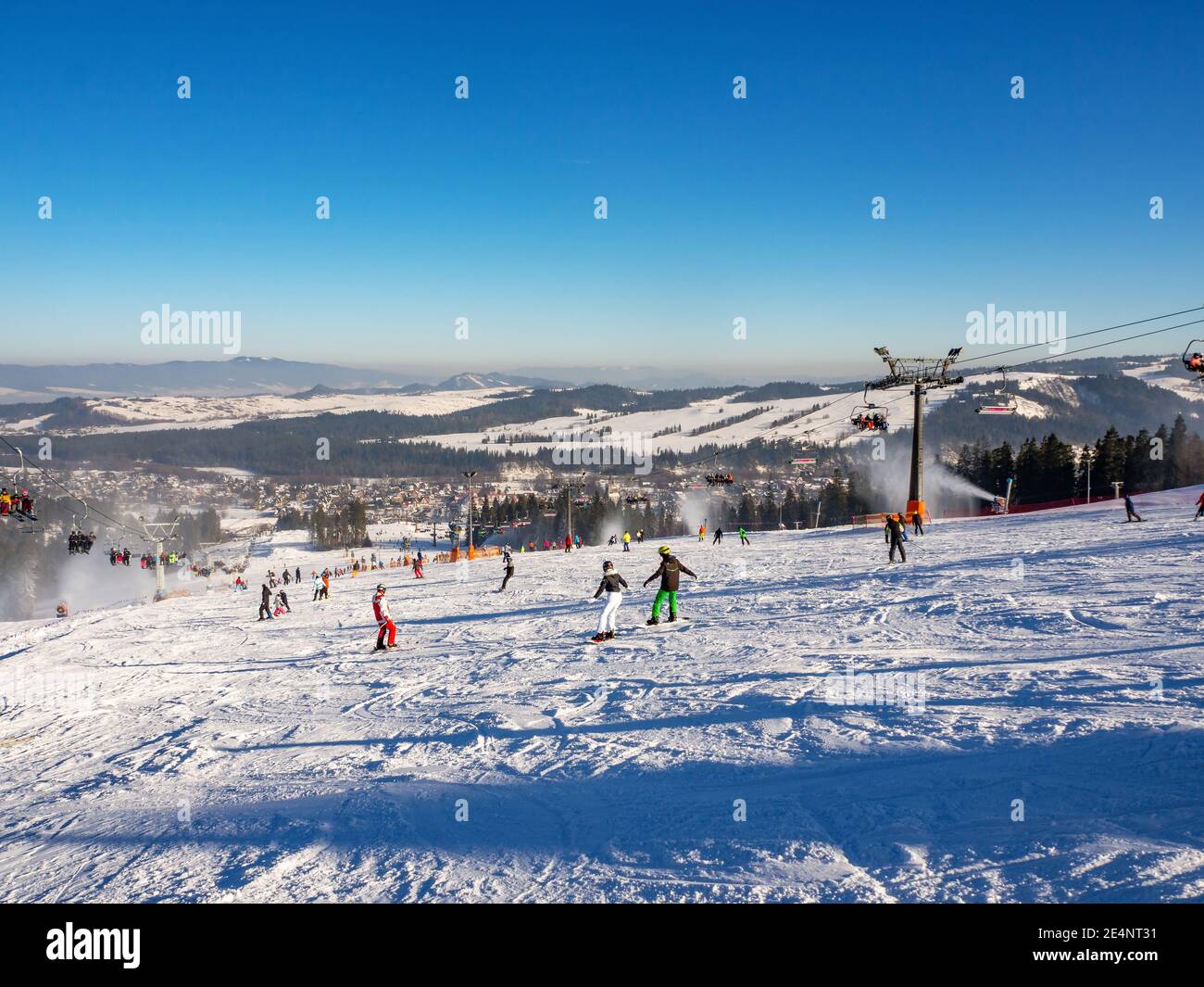 Skipisten, Sessellifte, Skifahrer und Snowboarder im Skigebiet Bialka Tatrzanska in Polen im Winter. Schneekanonen in Aktion Stockfoto