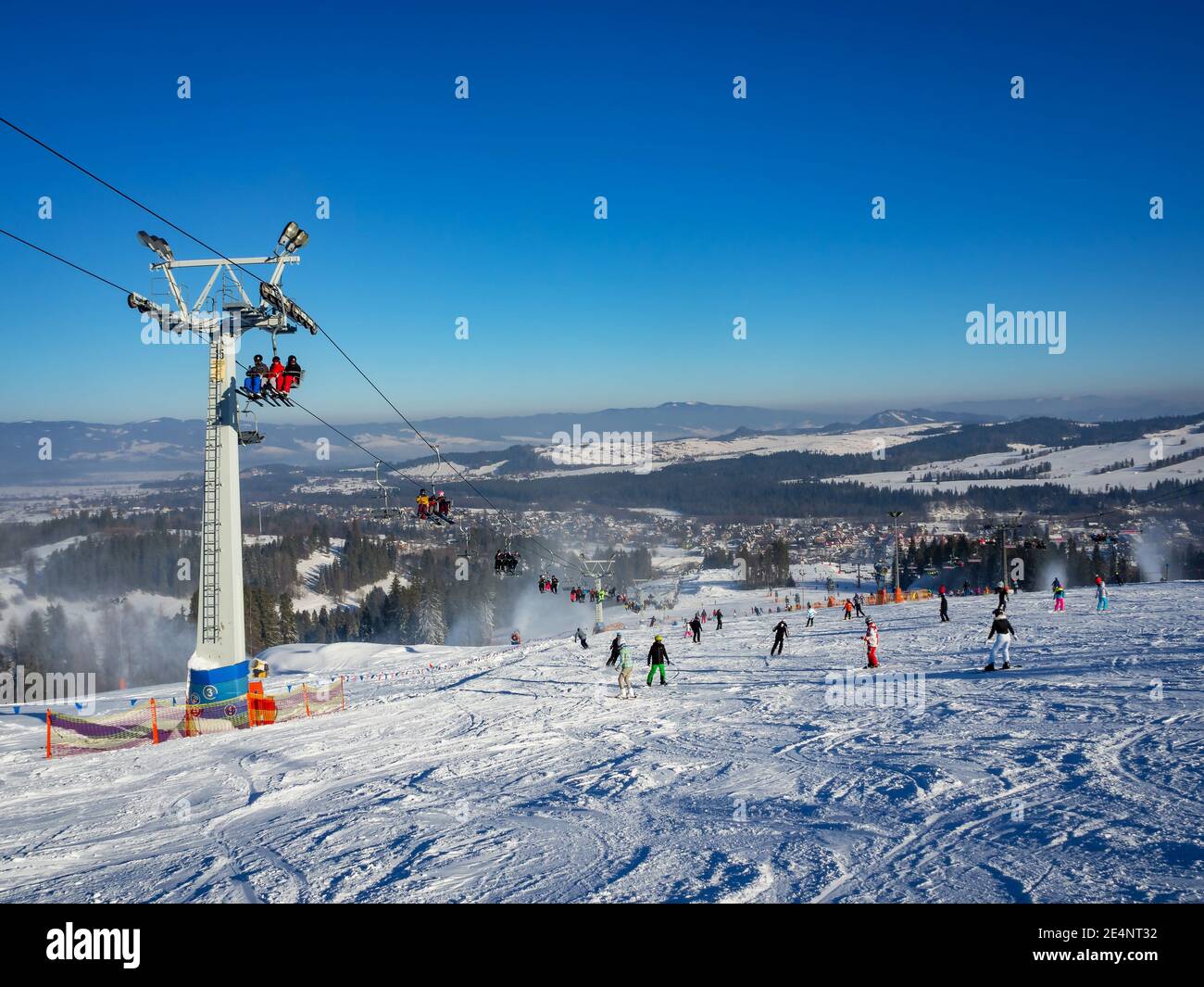 Skipiste, Sessellift, Skifahrer und Snowboarder im Skigebiet Bialka Tatrzanska in Polen im Winter. Schneekanonen in Aktion Stockfoto