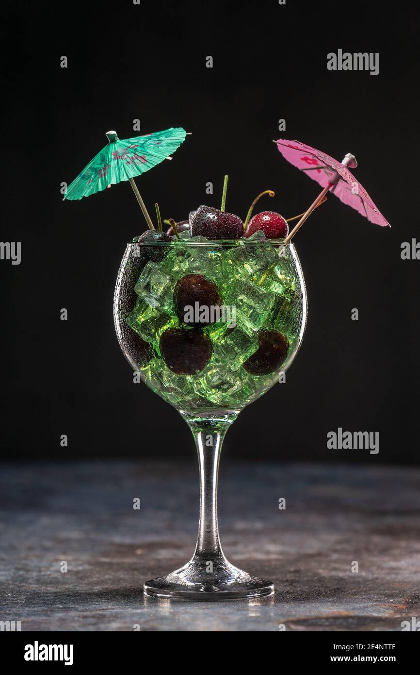 Grüner Cocktail mit Eis und Kirschen in einem Glas dekoriert Mit Sonnenschirmen Stockfoto