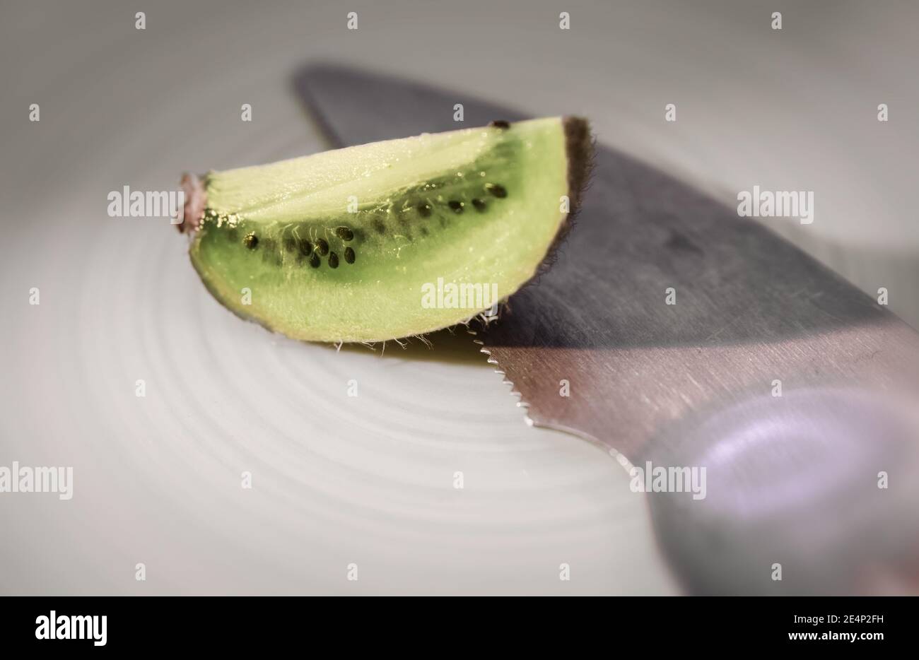Ein Stück Kiwifruit auf einem Teller, ein Küchenwerkzeug, um die Früchte zu essen, gibt es auch. Stockfoto