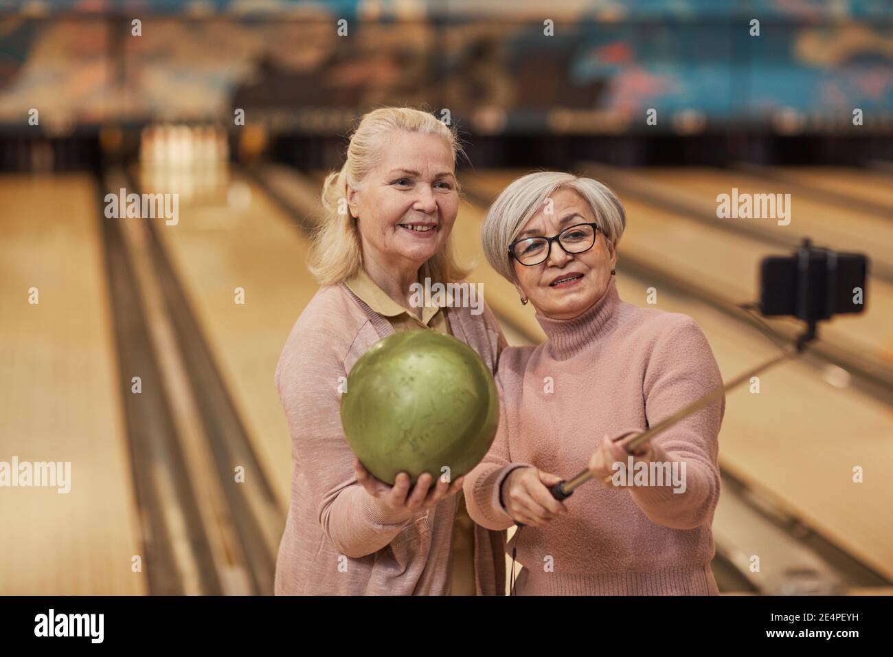 Waist-up-Porträt von zwei älteren Frauen, die Selfie-Fotos beim Bowling spielen und genießen Sie aktive Unterhaltung in Bowlingbahn, Kopierer Platz Stockfoto