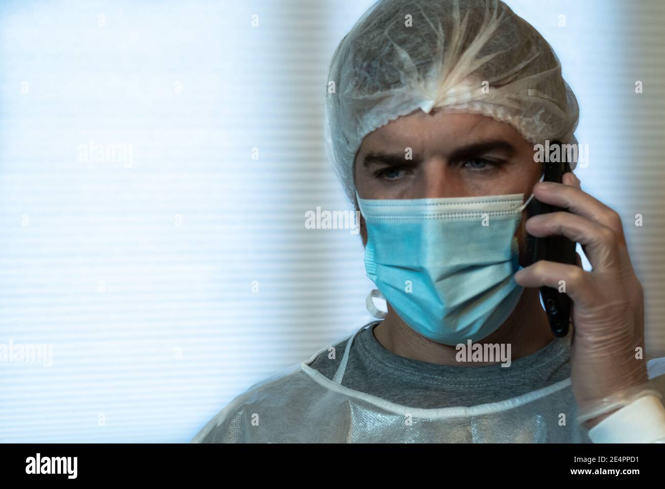 Ein Arzt spricht am Telefon mit einem besorgten Gesichtsausdruck, der in persönlicher Schutzausrüstung (PSA) gekleidet ist. COVID-19 Konzept Stockfoto