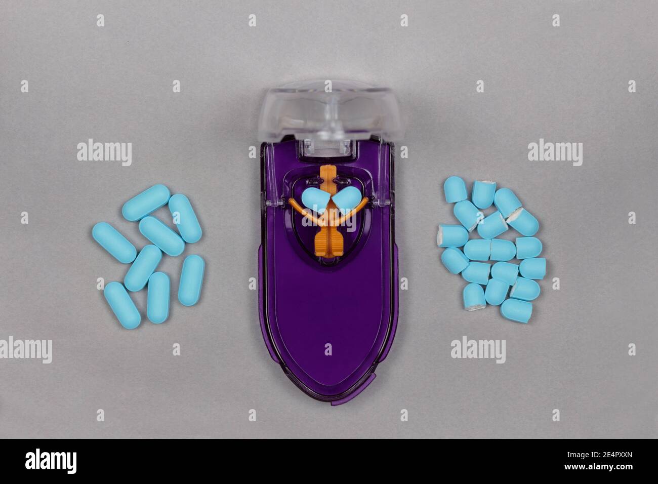 Ein lilafarbener und oranger Pillenschneider mit einer blauen Pille Unter der Klinge halb einschneiden und einen Stapel auflegen Ganze Pillen auf einer Seite und ein Stapel geschnitten Pillen auf der Hafer Stockfoto