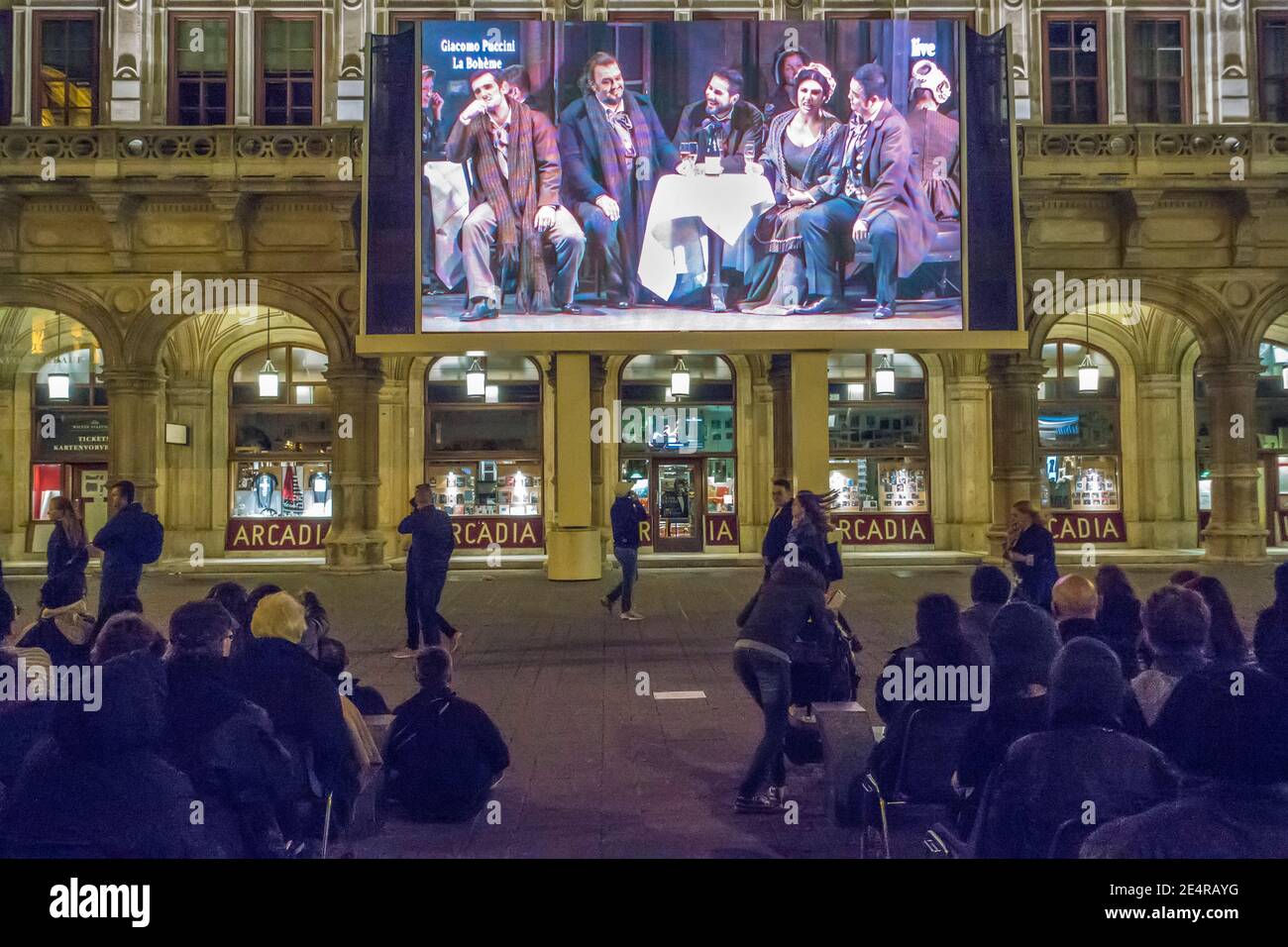 Personen, die vor der Wiener Staatsoper oder der Wiener Staatsoper sitzen Haus sehen eine Leistung kostenlos auf einem Outdoor-Bildschirm Stockfoto
