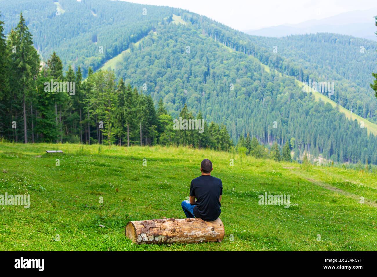 Kerl sitzt auf Holz und genießen Sie friedliche grüne Berglandschaft. Ruhe und Entspannung. Stockfoto