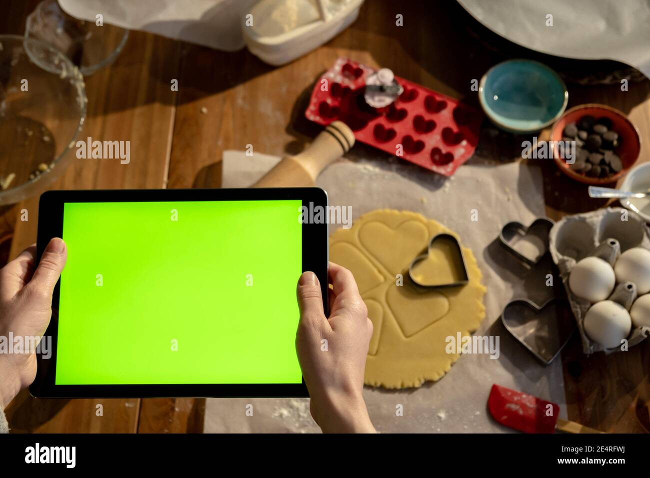 Frau hält Tablet mit grünem Bildschirm in der Hand Uhren Bildung. Cookie Zutaten im Hintergrund. Stockfoto