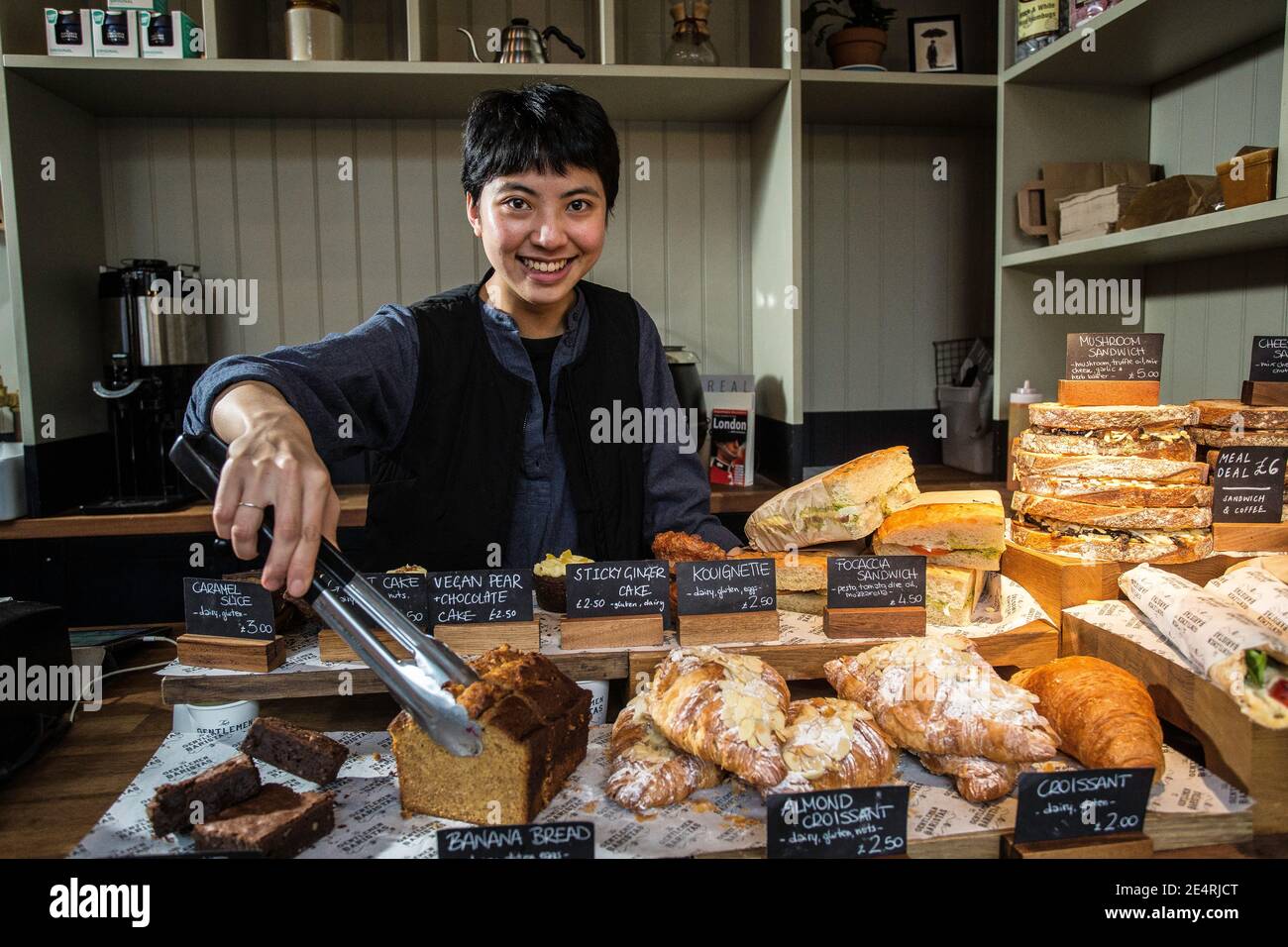 Attraktive Barista lächelt am Bäckereitisch und schlägt Kuchen in einem modernen Café oder Restaurant vor. Stockfoto