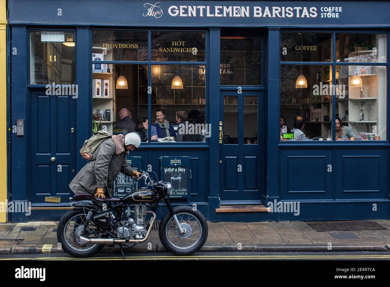 Ein Mann kommt mit einem klassischen Motorrad in einem Café in London an. Stockfoto