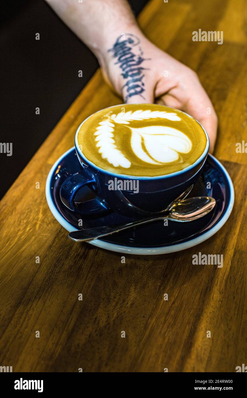 GROSSBRITANNIEN / England / London/Hand mit Tatoo, die Kaffee hält cup in einem Indoor-Café in London.Nahaufnahme der Hände Tasse Kaffee halten Stockfoto