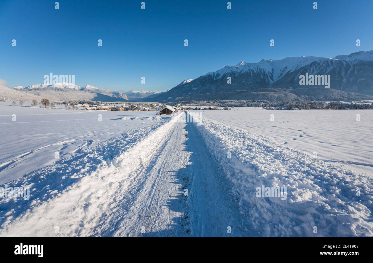 Schneebedeckter Wanderweg durch sonnige alpine Winterlandschaft zum Dorf Wildermieming, Tirol, Österreich Stockfoto