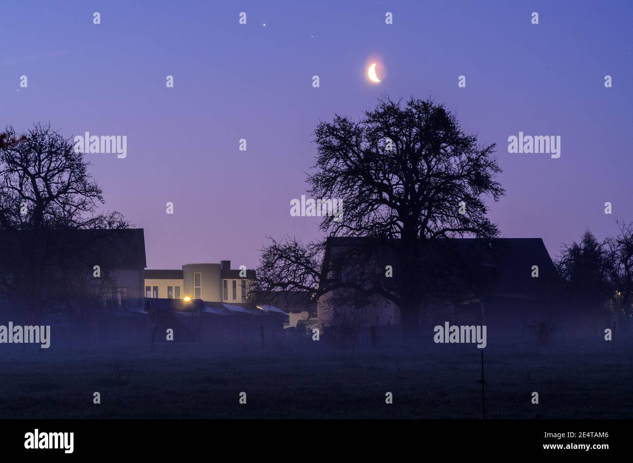 Früher nebliger Morgen auf dem Dorf auf dem Land mit Mond und Planeten am Himmel Stockfoto