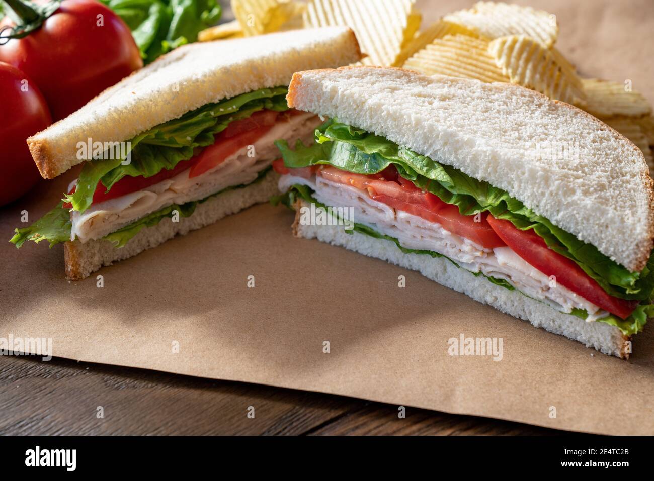 Frischer truthahn, Salat und Tomatenbrot, halbiert auf braunem Papier Stockfoto