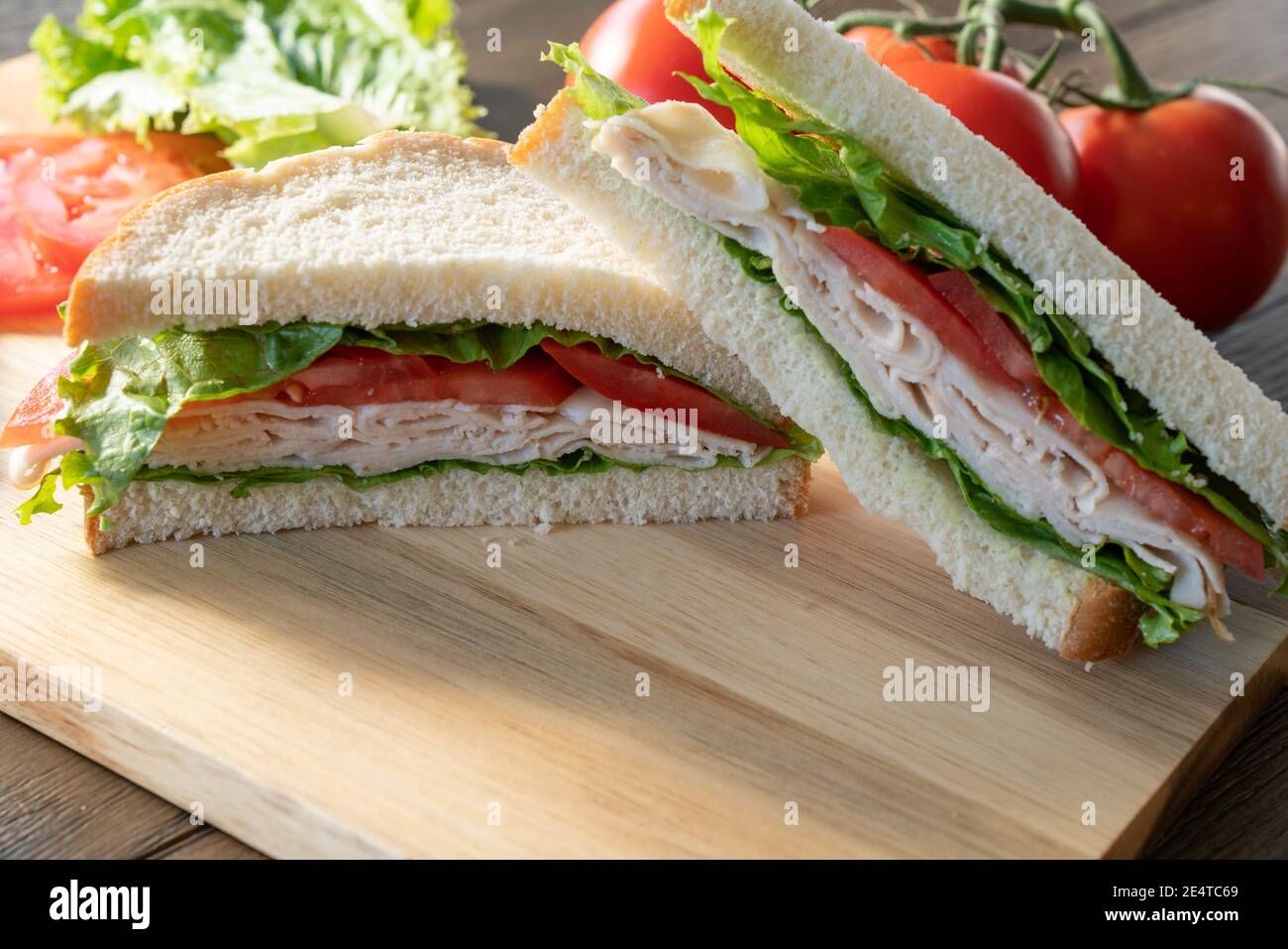 Frischer truthahn, Salat und Tomatenbrot, halbiert auf Schneidebrett Stockfoto