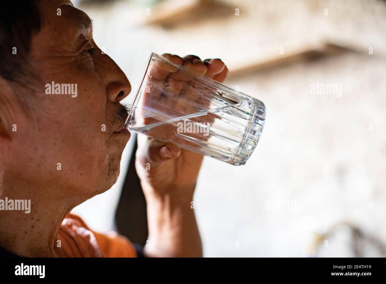 Ein älterer Mann trinkt ein Glas sauberes Wasser in seinem Haus in San Juan la Laguna, Guatemala, Mittelamerika. Stockfoto