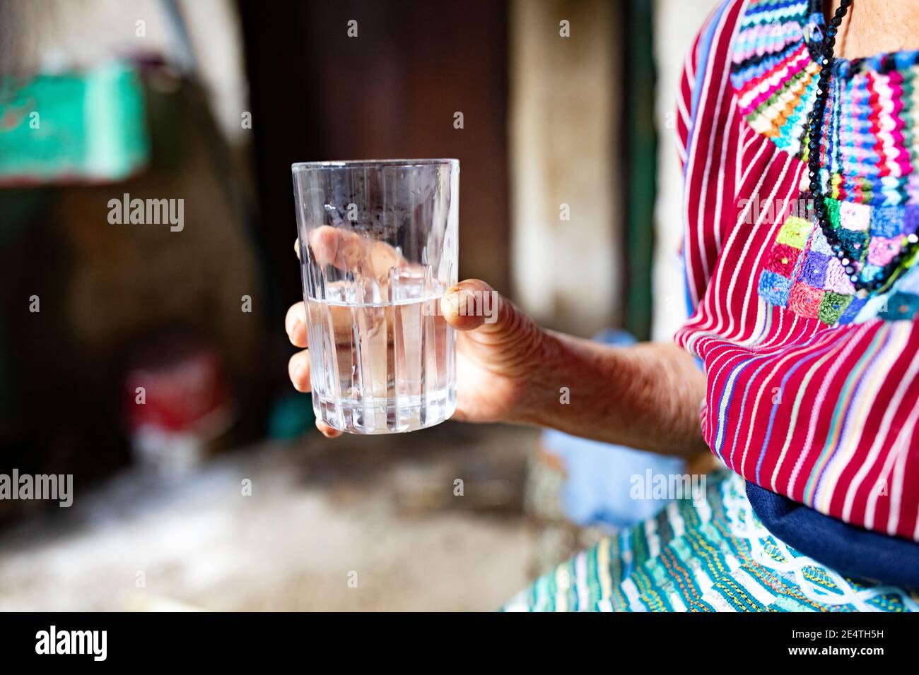 Eine ältere Frau trinkt ein Glas sauberes Wasser in San Juan la Laguna, Guatemala, Mittelamerika. Stockfoto