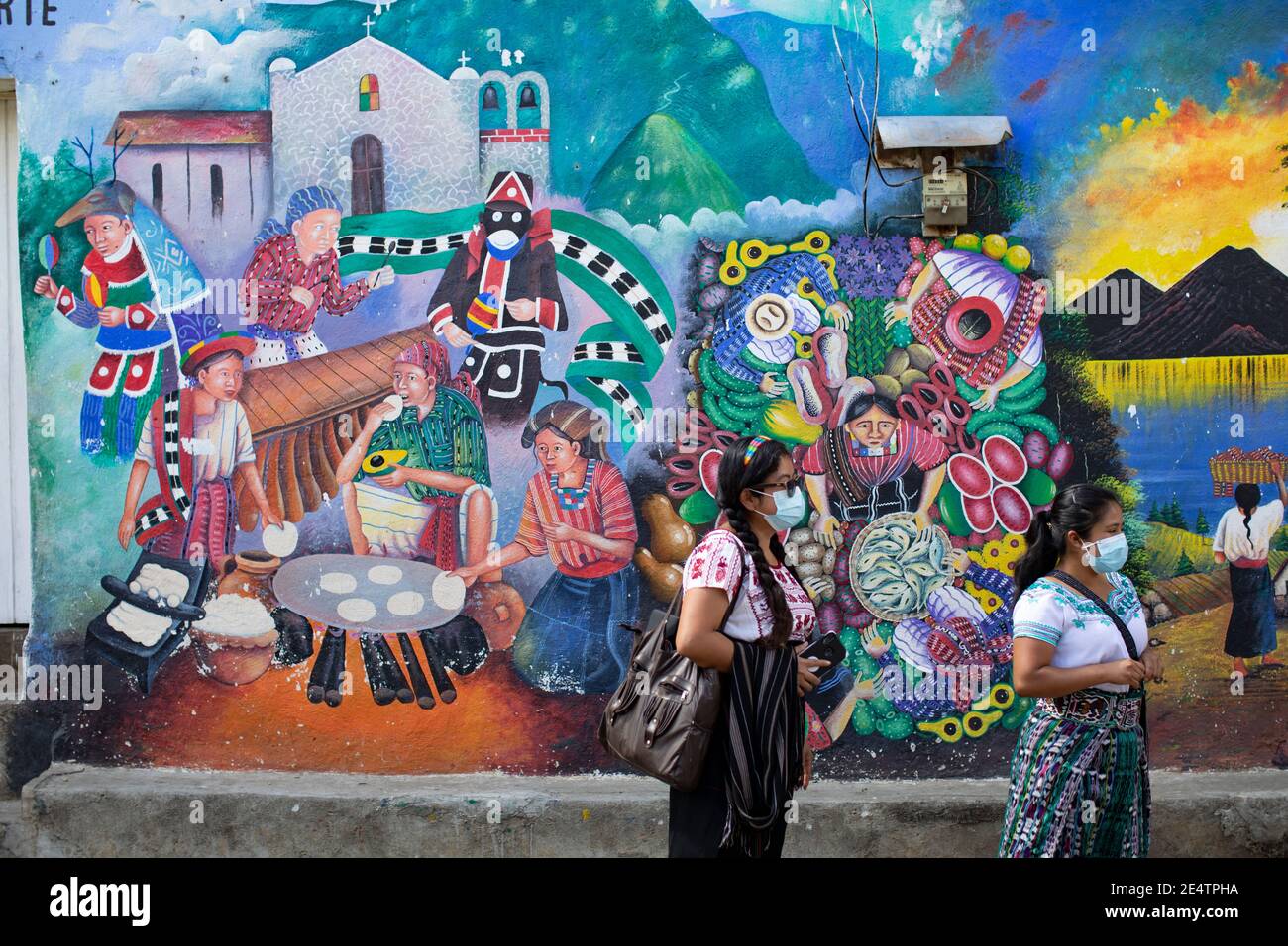 Frauen in Schutzmasken stehen vor einem Wandbild in San Juan la Laguna, Guatemala, Mittelamerika. Stockfoto