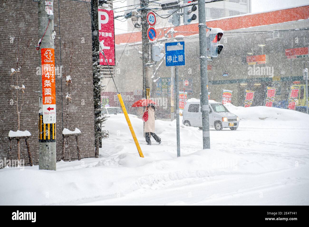 Eine Fußgängerin mit einem roten Regenschirm, die während eines Schneesturms in der japanischen Stadt läuft. Stockfoto